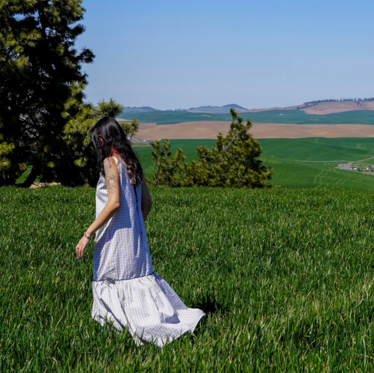 Woman in a white dress standing in a green field with rolling hills in the background